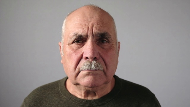 近距离的头和肩膀视频肖像的一个秃顶的老男人与胡子看着相机和向右和向左与一个悲伤和沮丧的面部表情对灰色背景的复制空间视频下载