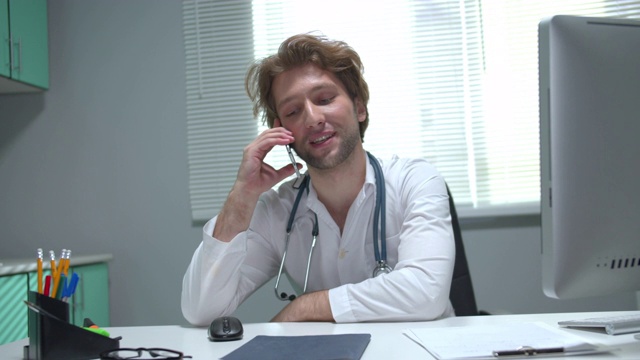医生坐在一张桌子在医院的内阁和交谈电话友好视频素材