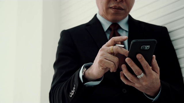 中年商人穿着黑色正装，打着领带，在手机上发短信视频素材