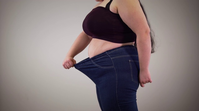 侧面的丰满的白人妇女显示可伸缩的牛仔裤。胖女孩在室内穿衣服。超重、肥胖、脂肪团。视频下载