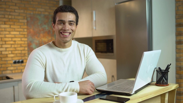 成功的年轻人对着镜头微笑，坐在笔记本电脑前，谈生意视频素材