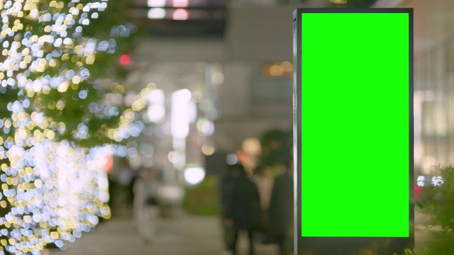 首都街头的夜间绿屏广告牌。慢镜头里有通勤者、行人和树上冬天的灯光。文本或副本的空间。视频素材