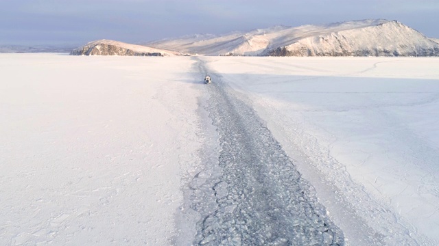 一艘船在结冰的湖面上留下的痕迹上方升起的无人机。冬天的风景视频素材