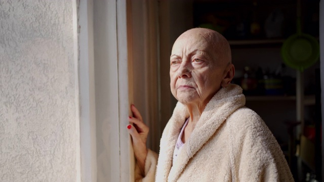 一位患有癌症和脱发的老年妇女，透过窗户往外看视频素材