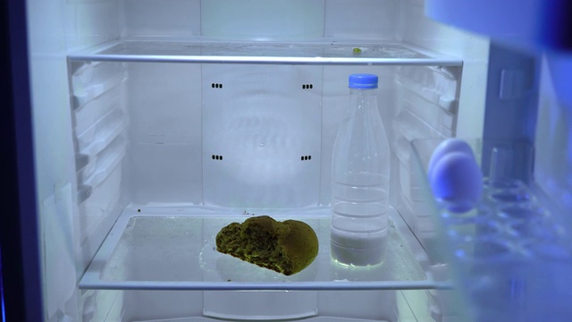 在冰箱里找食物的人。一个男人把牛奶和面包放进冰箱。视频下载