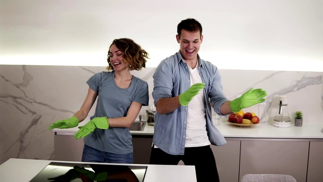 快乐的年轻夫妇在厨房里同步跳舞，都戴着绿色橡胶手套，在单间公寓里打扫卫生。有趣的动作。现代青年，人与家务观念视频素材