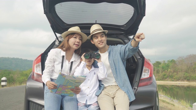 亚洲家庭的肖像坐在汽车与父亲指向的观点和母亲拿着地图与女儿看美丽的风景通过双筒望远镜在假期一起度假。幸福的家庭时间。视频下载