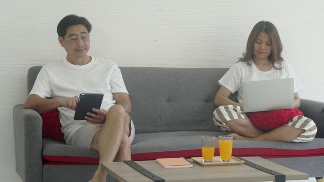 年长的亚洲夫妇在家里的沙发上工作，并不关心彼此。视频素材