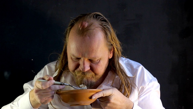 饥饿的胖子，穿着白衬衫留着长发，胡子在黑色的背景下，飞快地吃着一碗棕色的饭视频下载
