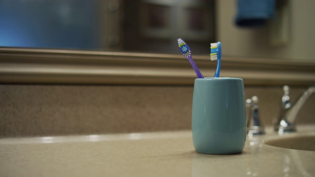CU浴室柜台和水槽;一个男人走了进来，他的手从杯子里抓了一把牙刷。然后把它放回去。视频下载