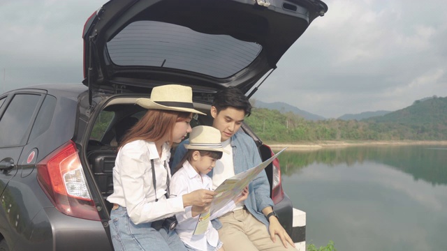 亚洲家庭的肖像坐在汽车与父亲指向的观点和母亲与女儿看美丽的风景和拿着地图在假期一起度假。幸福的家庭时间。视频下载
