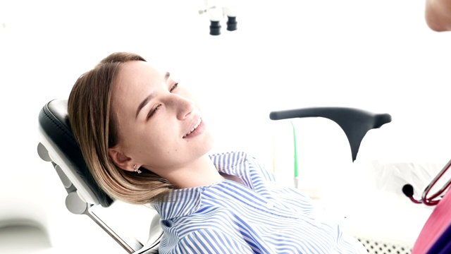 一个年轻的女孩坐在牙科诊所的椅子上，向一位戴眼镜的女牙医咨询。医生和病人的对话视频素材