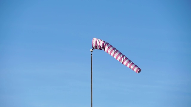 红色和白色的条纹表示风向和风速。在蓝天背景下发展的锥形风指示器。天气袜是由布料做成的截锥形视频素材