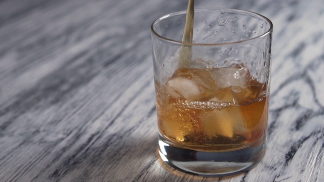 金色的威士忌倒进一个装有冰块的杯子里，放在一个旧的木制灰色吧台上视频素材