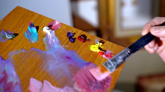 特写木色调色板与不同的油画颜料，熟练的女性艺术家混合颜色和创造新的色彩阴影在画布上绘制。专业的绘画工具，画刷视频下载