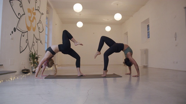 两个女人在一起练习瑜伽的慢动作视频，在轮子- urdhva dhanurasana姿势视频下载