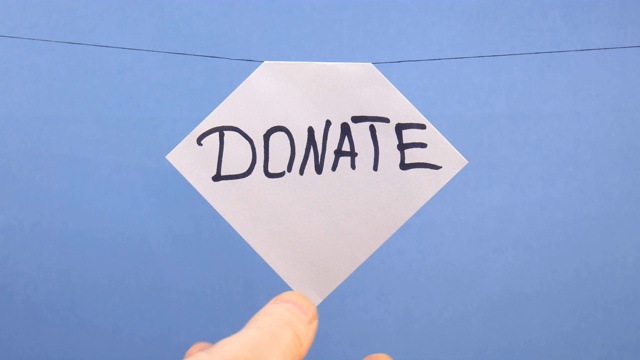 一名男子在蓝色背景上挂了一张白纸，上面写着黑色的“捐赠”字样视频下载