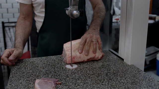 一个面目全非的男人在肉店用电刀切一块肉的特写视频素材