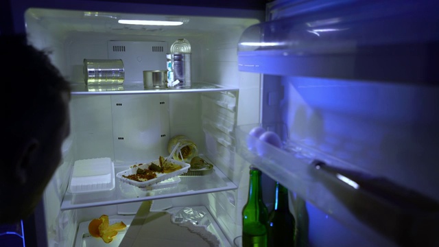 在冰箱里找食物的人。那人从冰箱里拿了披萨和一瓶啤酒。视频下载