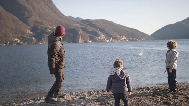 父亲教两个孩子如何在湖里打石子视频素材