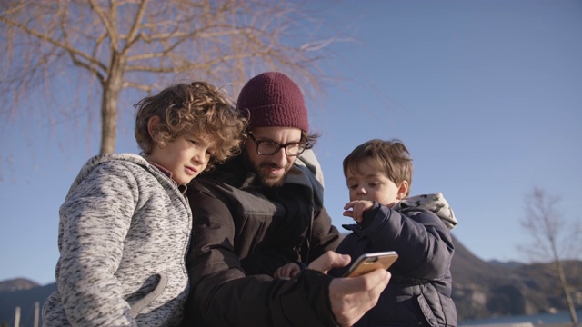 父亲和两个孩子在户外使用智能手机视频素材