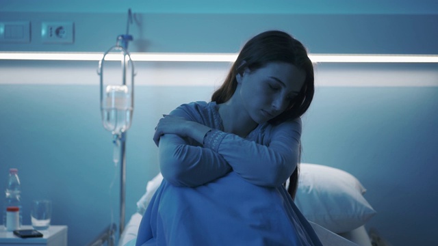 年轻的病人晚上坐在医院的病床上，感到悲伤视频素材