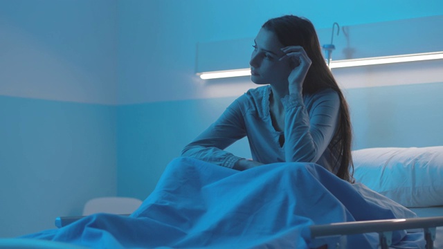 年轻的病人晚上坐在医院的病床上，感到悲伤视频素材