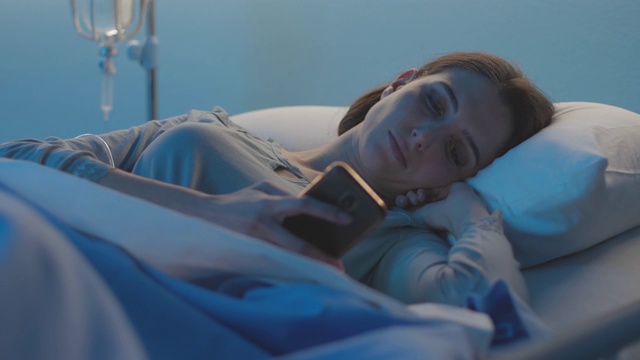 年轻的病人躺在病床上和她的电话聊天视频素材