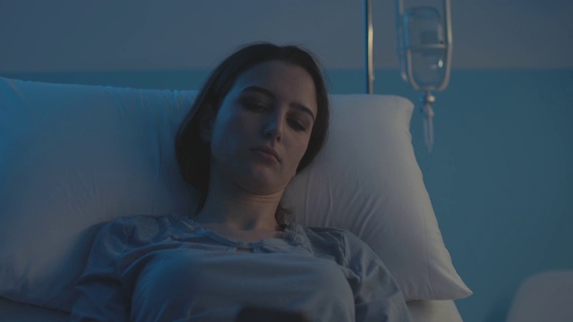 一个可怜的女人晚上躺在医院病床上用手机聊天视频素材