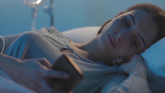 年轻的病人躺在病床上和她的电话聊天视频素材