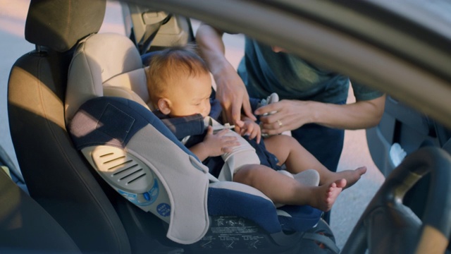 亚裔父亲把儿子放在汽车座椅上，慢镜头视频素材