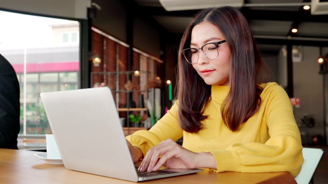 年龄在30-40岁之间的亚洲女性，穿着休闲装坐在咖啡厅或café共同工作空间。视频素材
