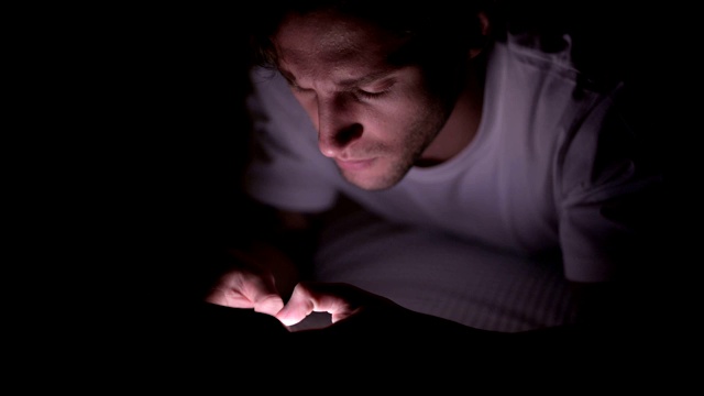 年轻人晚上在床上使用智能手机视频下载