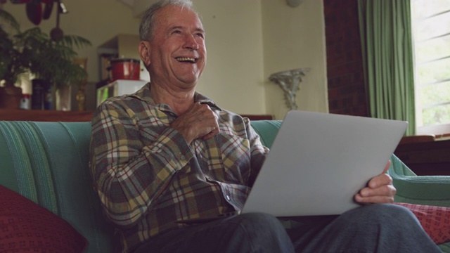 老人微笑着在家里用笔记本电脑视频下载