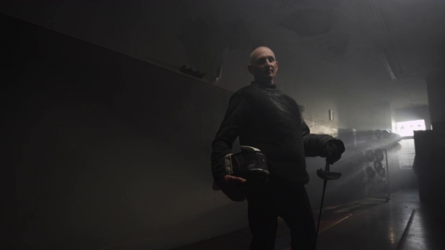 一名身穿黑色击剑服的老人在一个黑暗而多雾的体育馆摆姿势视频下载