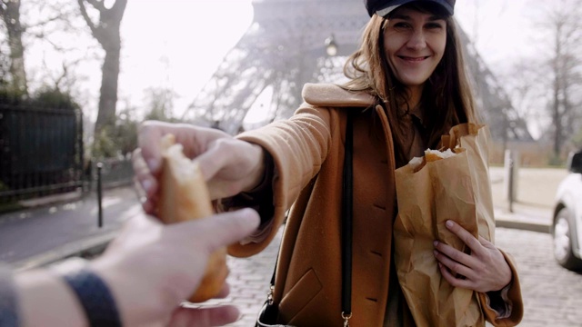 微笑的白人妇女走在巴黎埃菲尔铁塔，给一块法国面包给操作员慢动作。视频素材
