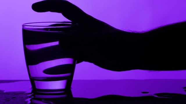 手抓满水的玻璃杯，洒出一些水紫色的背景视频下载