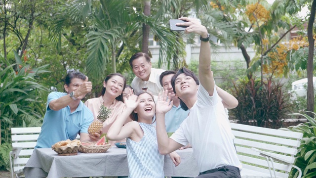 多代东南亚家庭在视频会议的同时享受户外花园派对视频素材