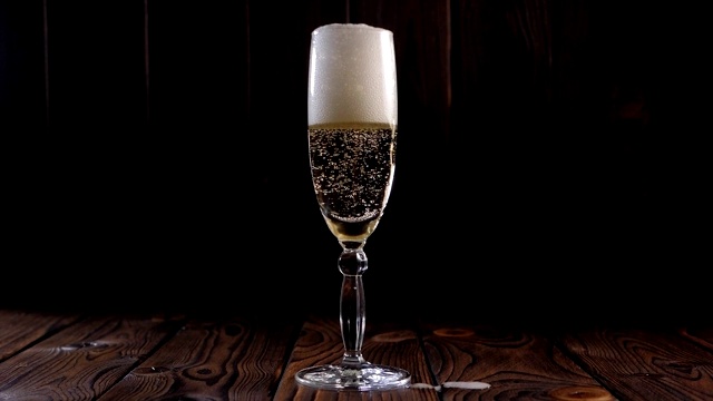 特写的香槟倒进一个玻璃杯在一个木制的背景，慢动作。视频下载