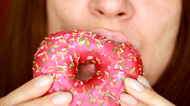 女人吃着粉色的甜甜圈，好吃，甜，爱吃甜食。饮食。节食。女嘴里咬着甜点。有选择性的重点视频素材