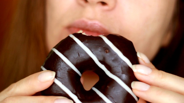 近距离的女人吃巧克力甜甜圈，好吃，甜，爱吃甜食。饮食。节食。女嘴里咬着甜点。有选择性的重点视频素材