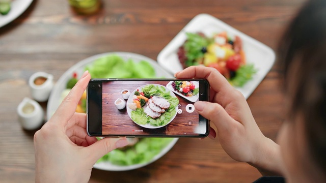 俯视图女性使用智能手机拍摄食物的盘子上的照片。用RED摄像机拍摄4K视频素材