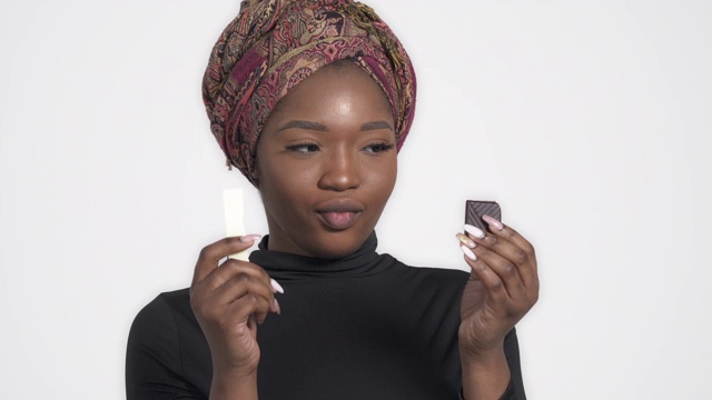 年轻迷人的非洲女子在白巧克力和黑巧克力之间选择。孤立，在白色背景上视频素材