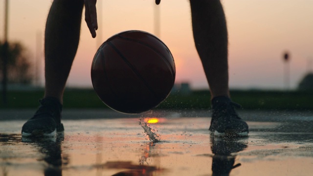 日落时分，男子在户外篮球场的水坑里弹跳篮球视频下载