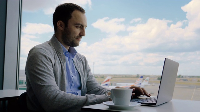一名男子在机场商务休息室的咖啡厅里用笔记本电脑工作视频下载