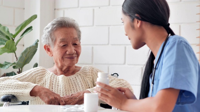 亚洲老年妇女听年轻的黑人女护士医生解释药物给她年长的女性病人在家。采购产品医疗，护理，护理，退休，志愿者，慈善，教育，养老院，在家照顾者，医药和卫生保健视频素材