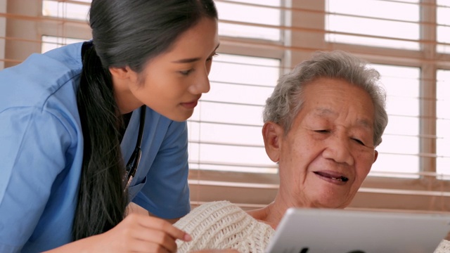亚洲老年妇女与年轻的黑人女护士医生交谈，帮助患者在家里进行平板电脑治疗Covid-19病毒的教育。教育、医疗、护理、技术、老年护理、退休、志愿者、养老院、冠状病毒或Covid-19，家庭护理人员视频下载
