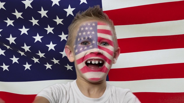 以美国国旗为背景的快乐的扇子。快乐的男孩，脸上涂着民族色彩。视频下载