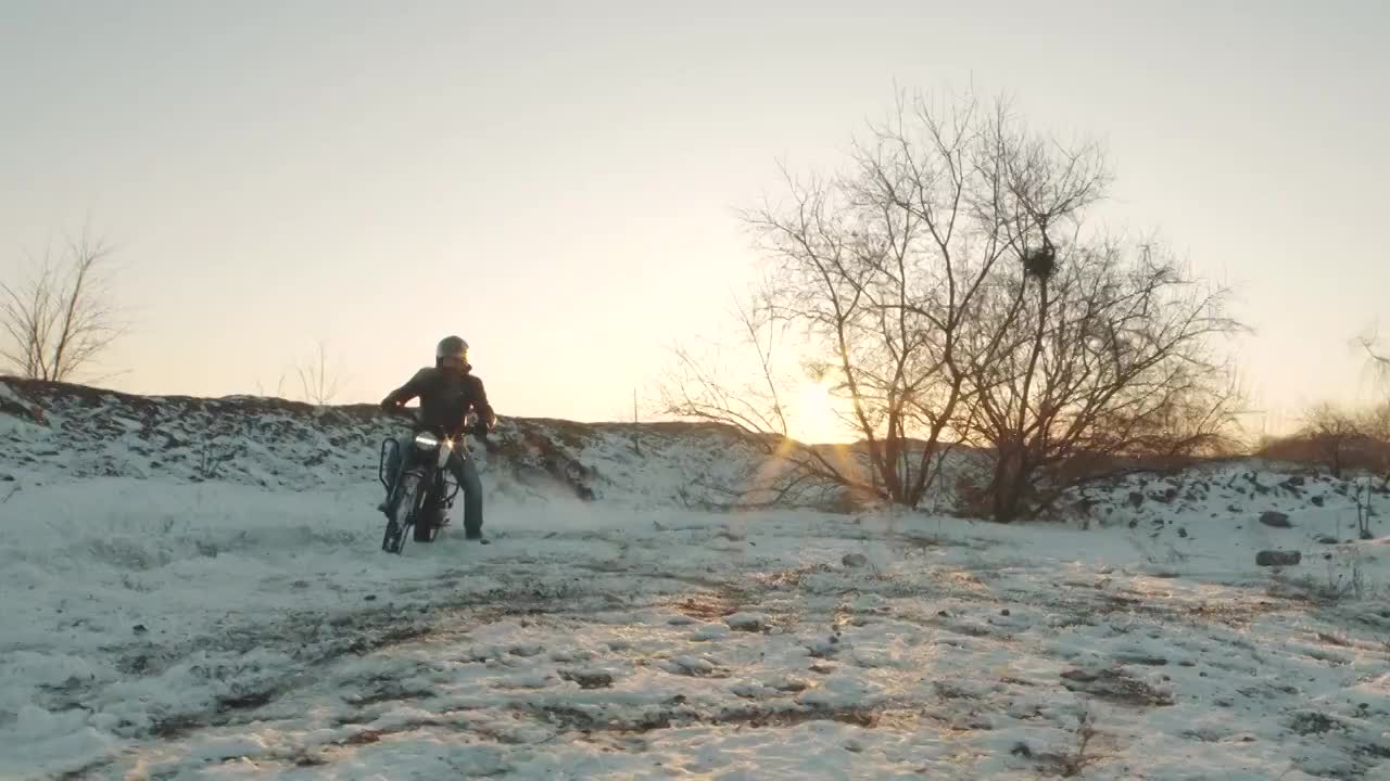 摩托车手在雪地上轮胎烧坏，慢镜头。夕阳西下，专业的摩托车手在雪地上滑行和转弯。骑摩托车的人在摩托车上表演特技视频素材