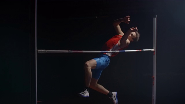 慢动作:男子运动员在聚光灯下的黑暗背景上错误跳高视频素材